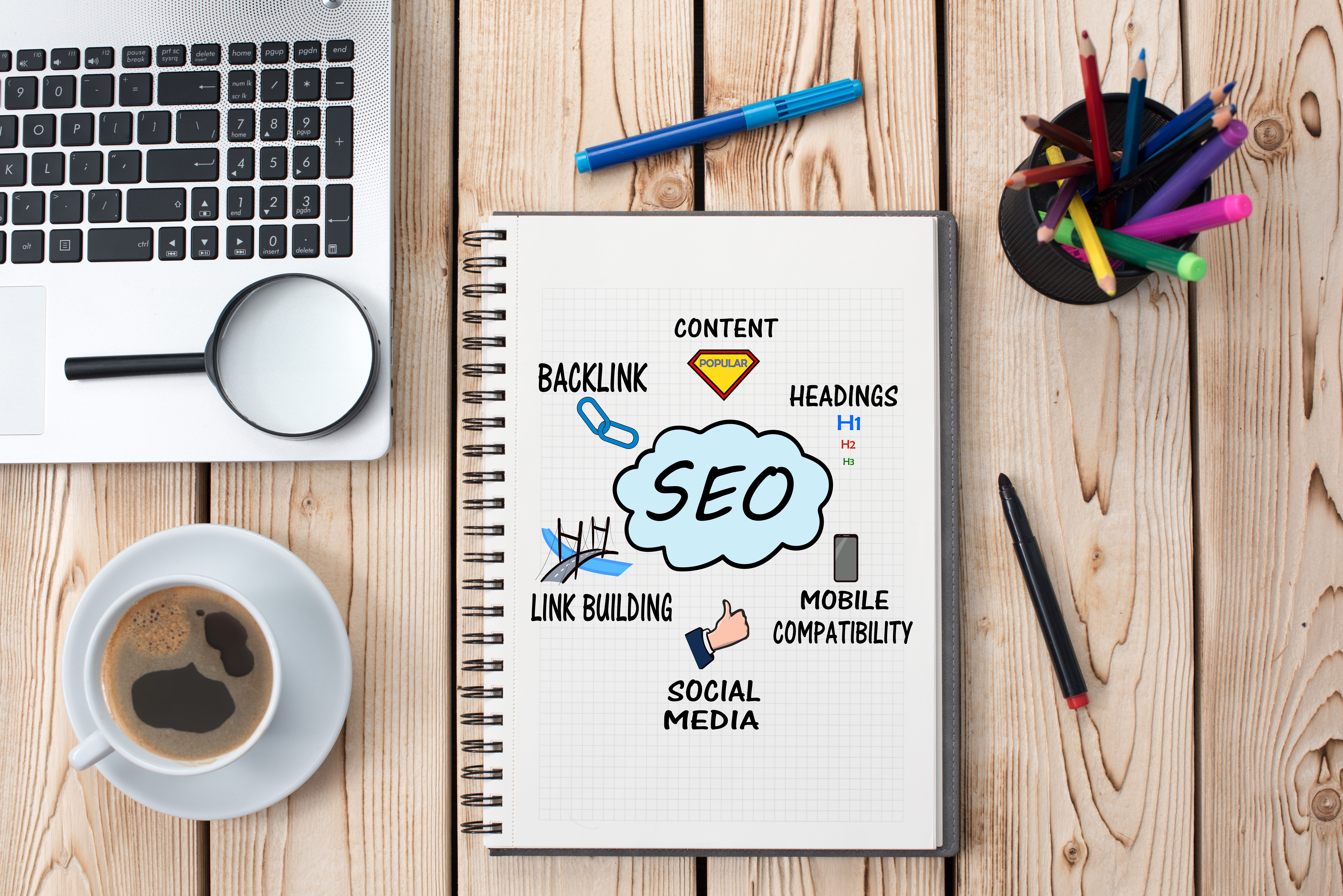 plan view of a workstation, desk, laptop, coffee cup, coloured pencils and notebook with SEO diagram